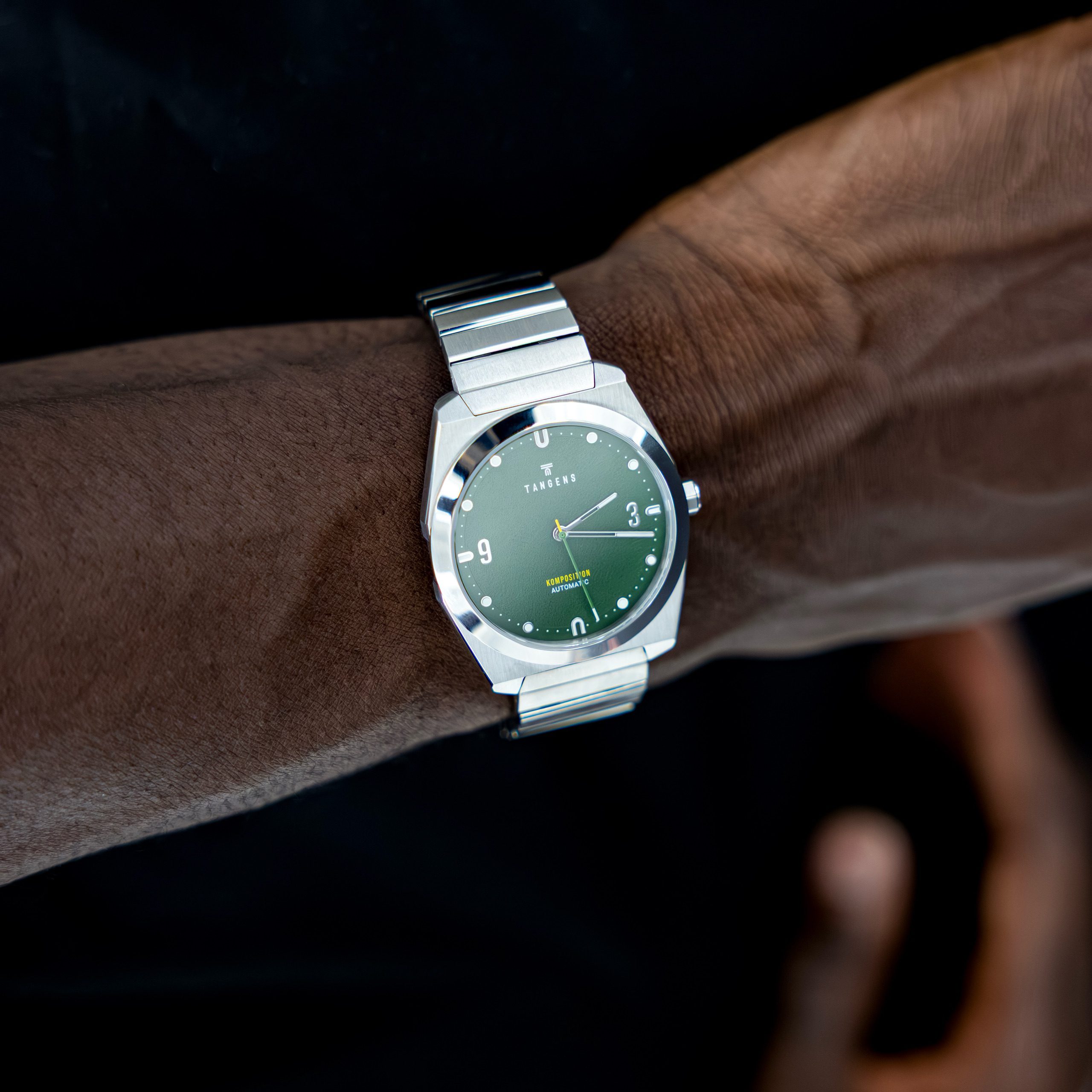A Komposition Automatic Juniper Green on a wrist against a black sweater