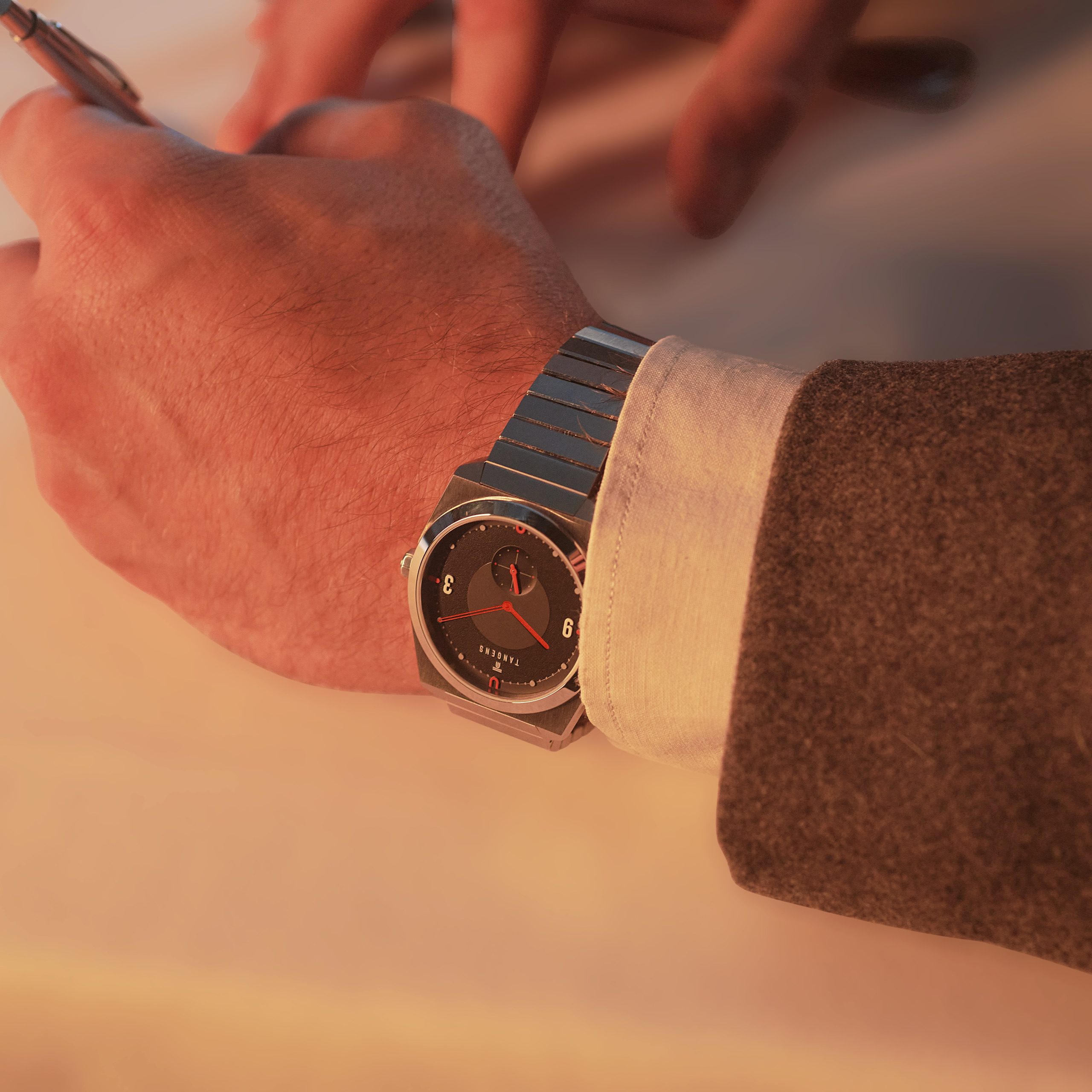 A Komposition Black on a wrist in a tweed sleeve, writing at a table