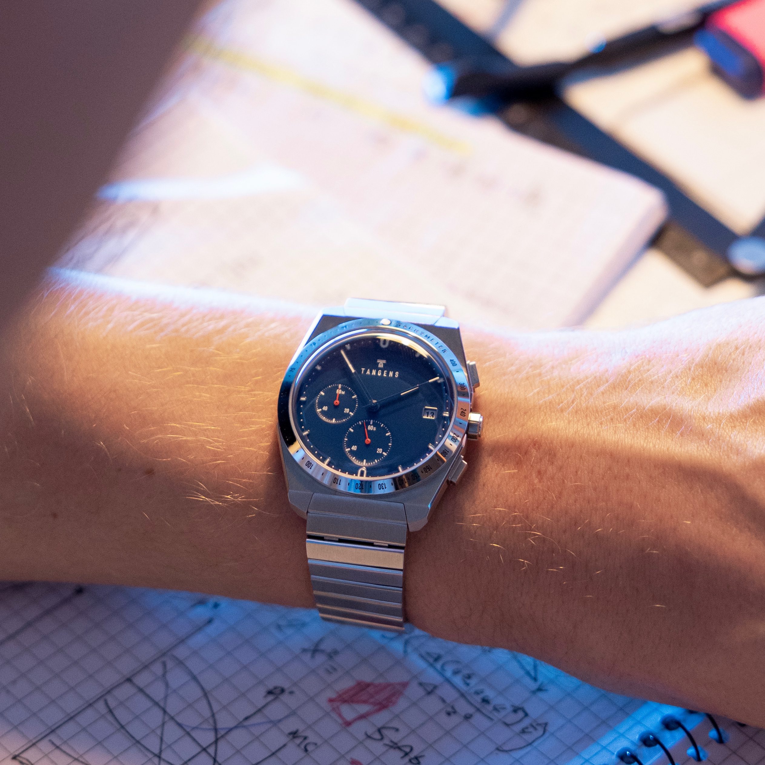A Komposition Chronograph Cool Navy on a wrist over a notebook of sketches