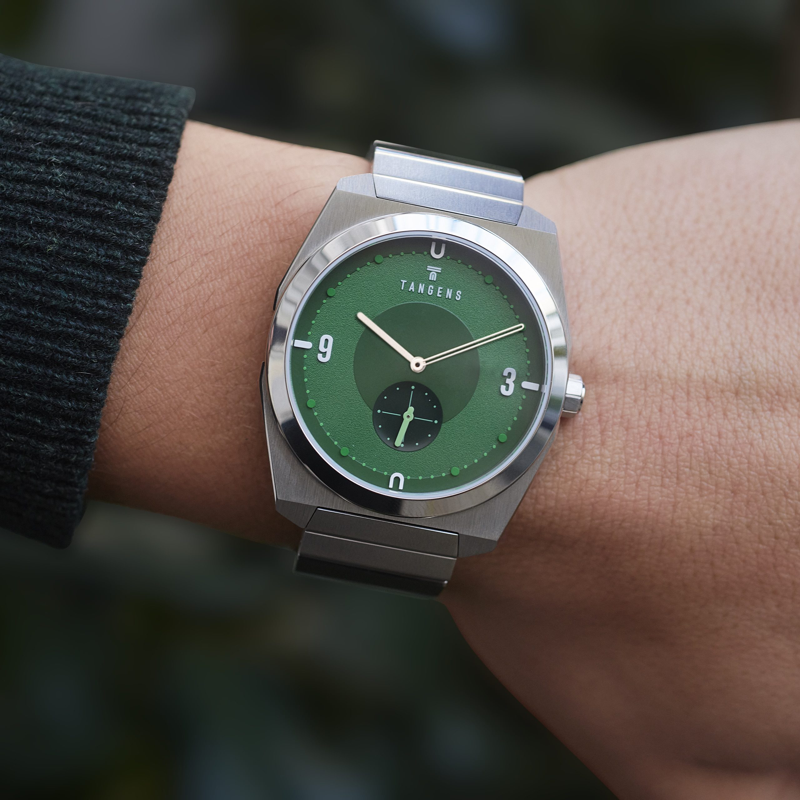 A Komposition Green on a wrist in a dark knit sleeve