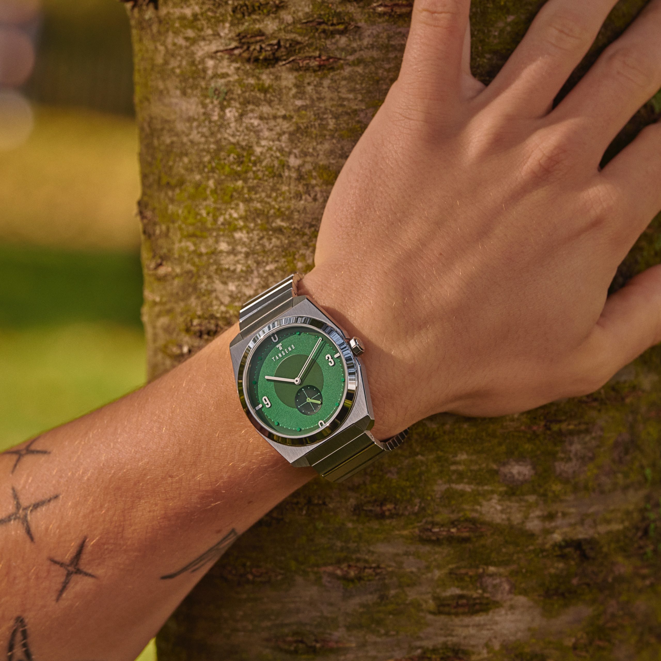 A Komposition Green on a wrist, the hand resting on a tree trunk